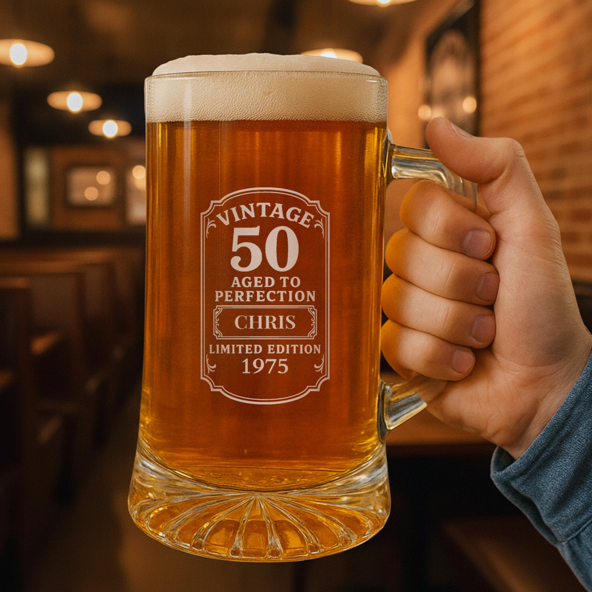 Hand holding a personalized 50th birthday beer stein in a warm pub, the Vintage 50 label engraved with the name Chris and the year 1975