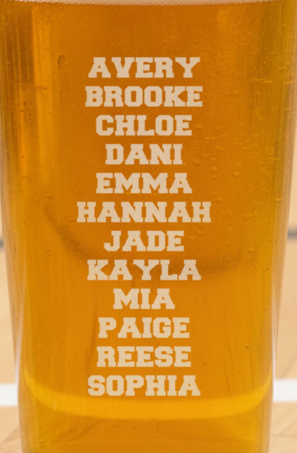 Back of the volleyball coach pint glass engraved with a twelve-name team roster from Avery to Sophia, stacked and centered on the glass
