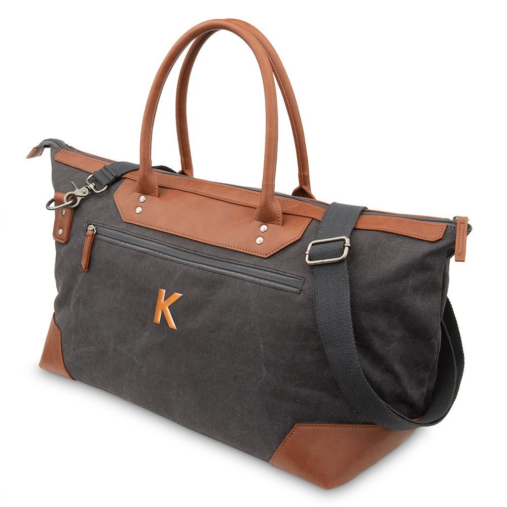 Large personalized canvas weekender travel bag in charcoal gray with brown faux leather handles and corners, the initial K embroidered in copper thread on the front